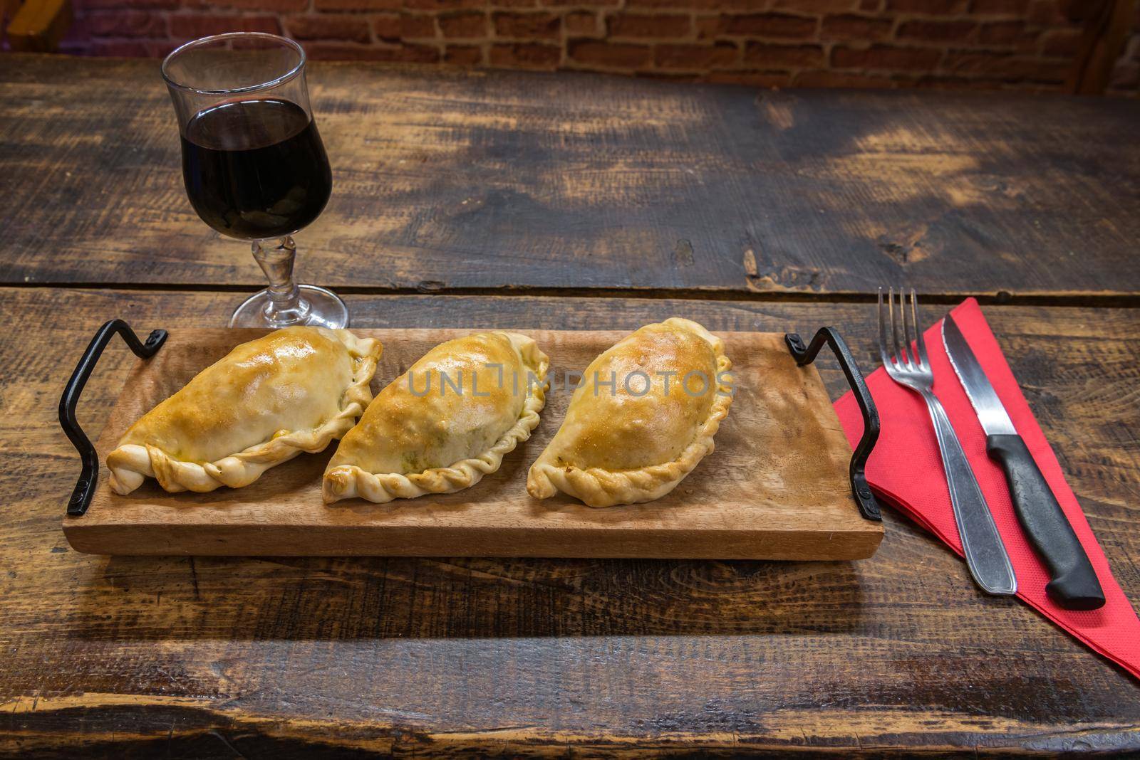 Traditional baked Argentine and Uruguay empanadas savoury pastries with meat beef stuffing against wooden background.