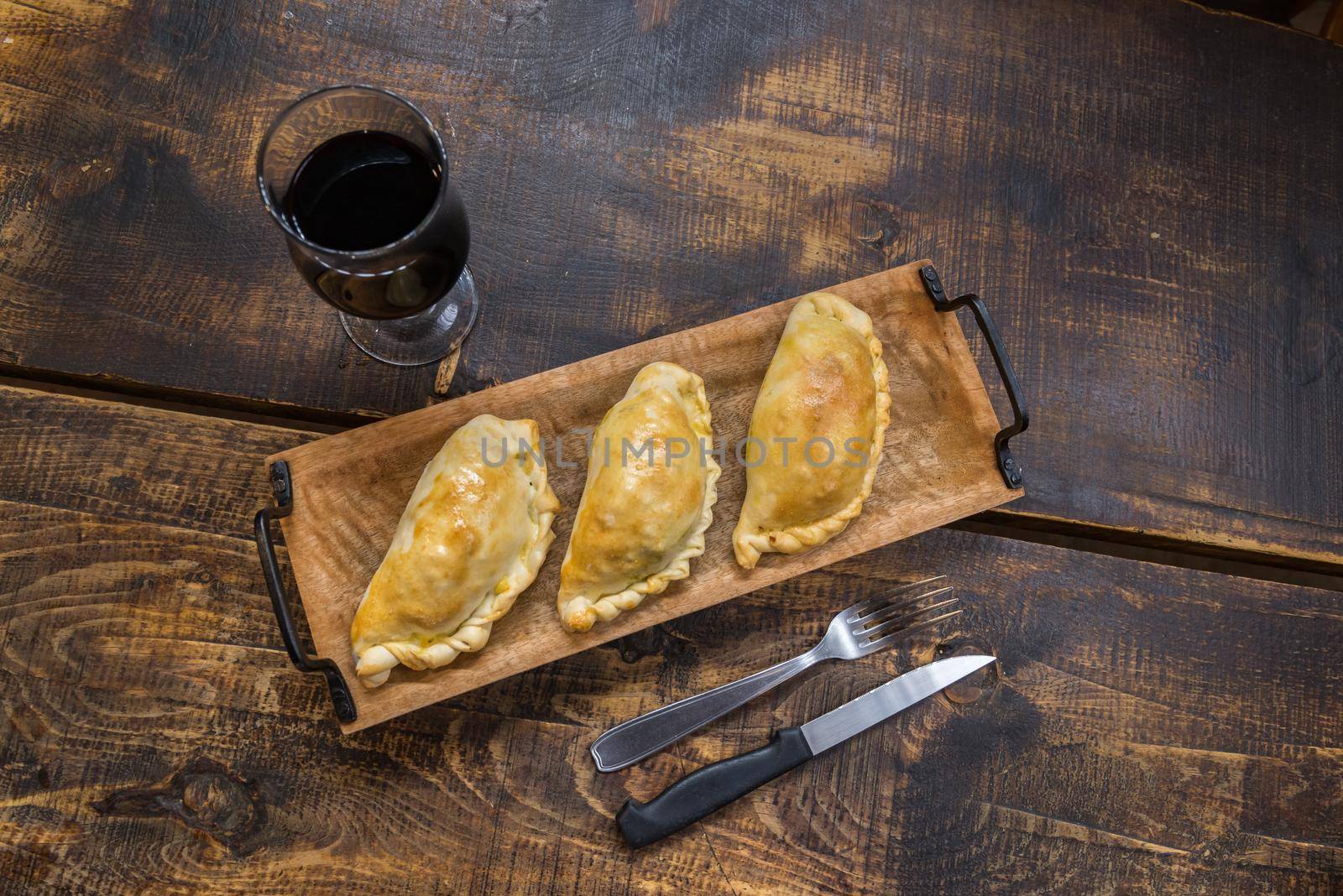 Traditional baked Argentine and Uruguay empanadas savoury pastries with meat beef stuffing against wooden background.