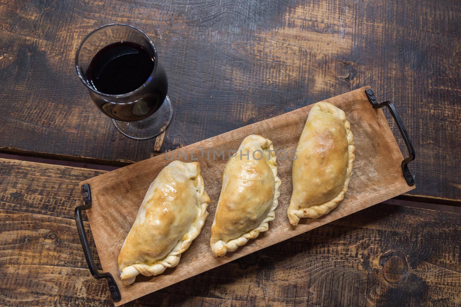 Traditional baked Argentine and Uruguay empanadas savoury pastries with meat beef stuffing against wooden background.