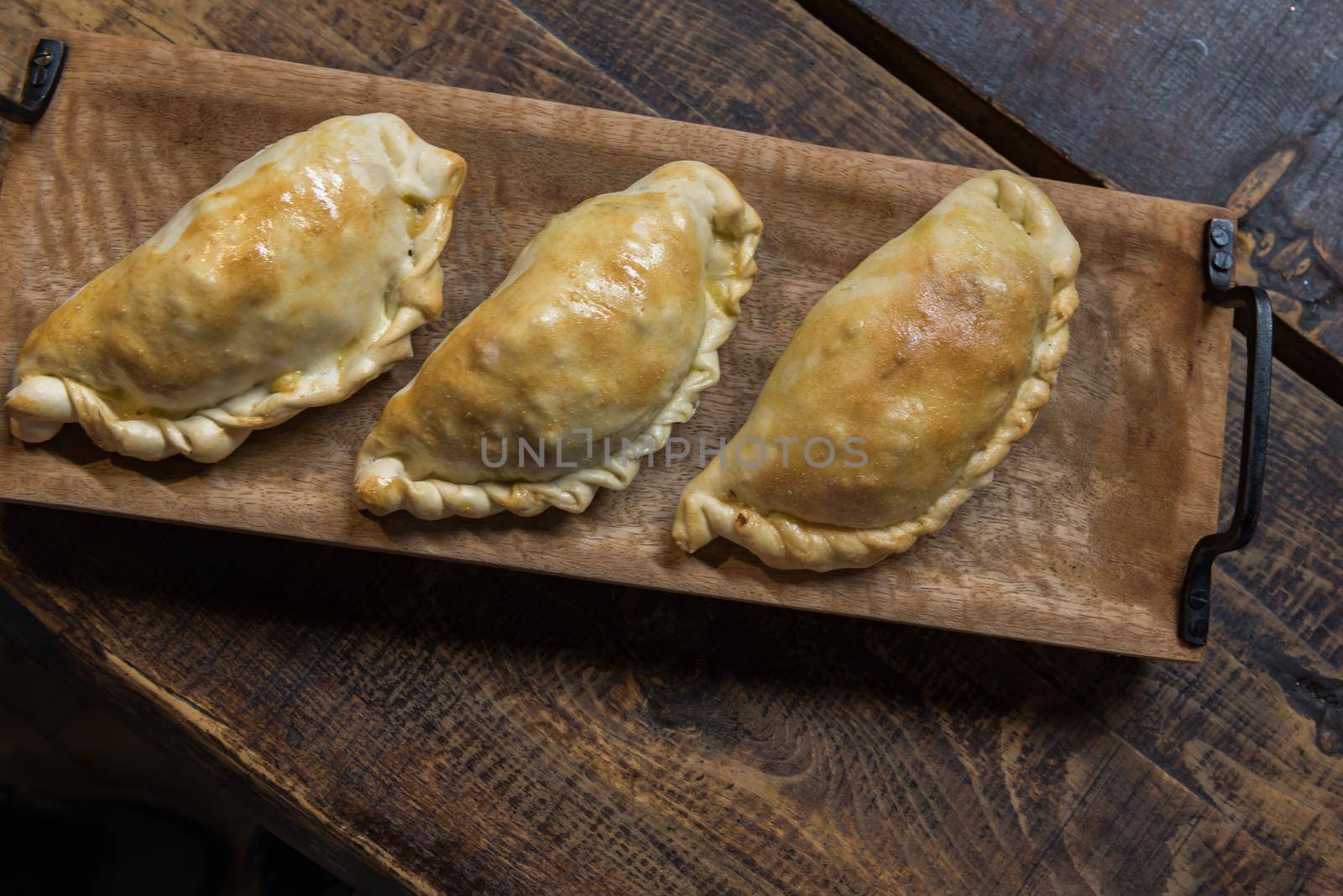 Traditional baked Argentine and Uruguay empanadas savoury pastries with meat beef stuffing against wooden background.