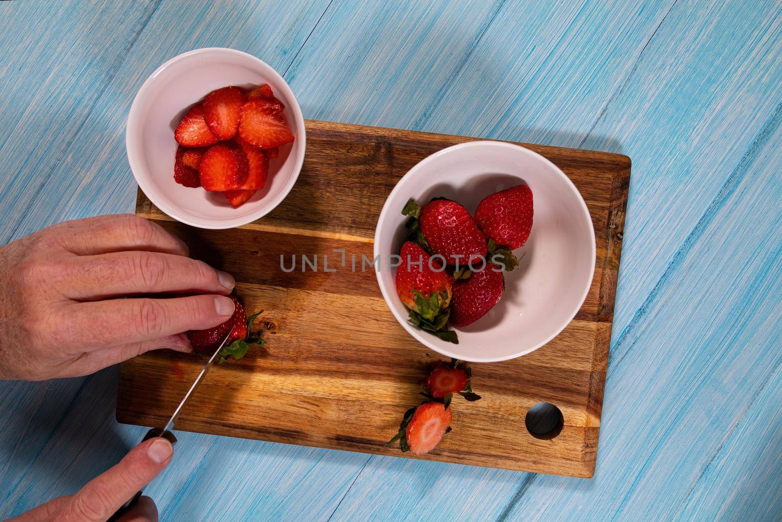Overhead view of a man slicing plump strawberries on a wooden cutting board.
