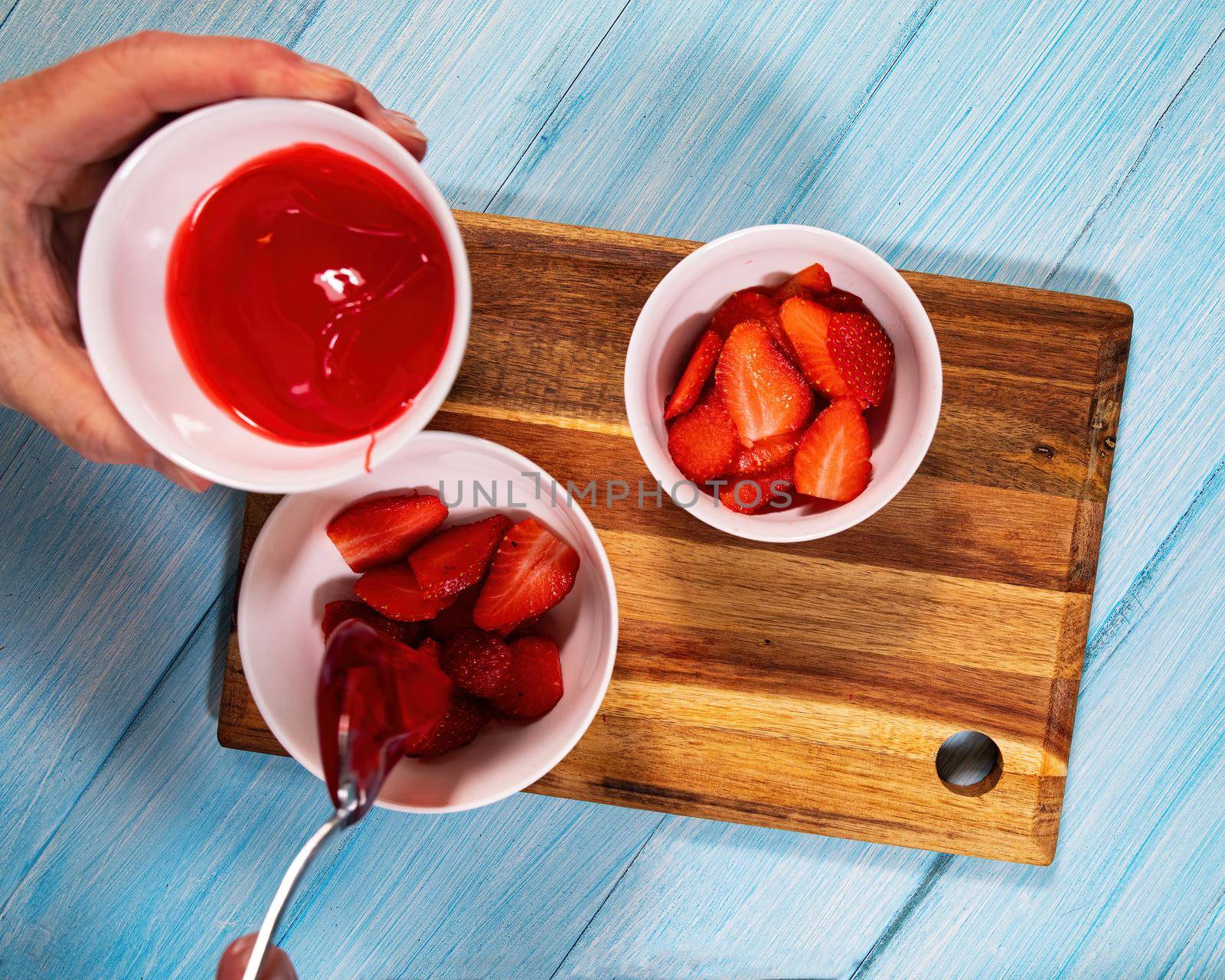 Sliced strawberries in white bowls with man adding fruit glaze to them.