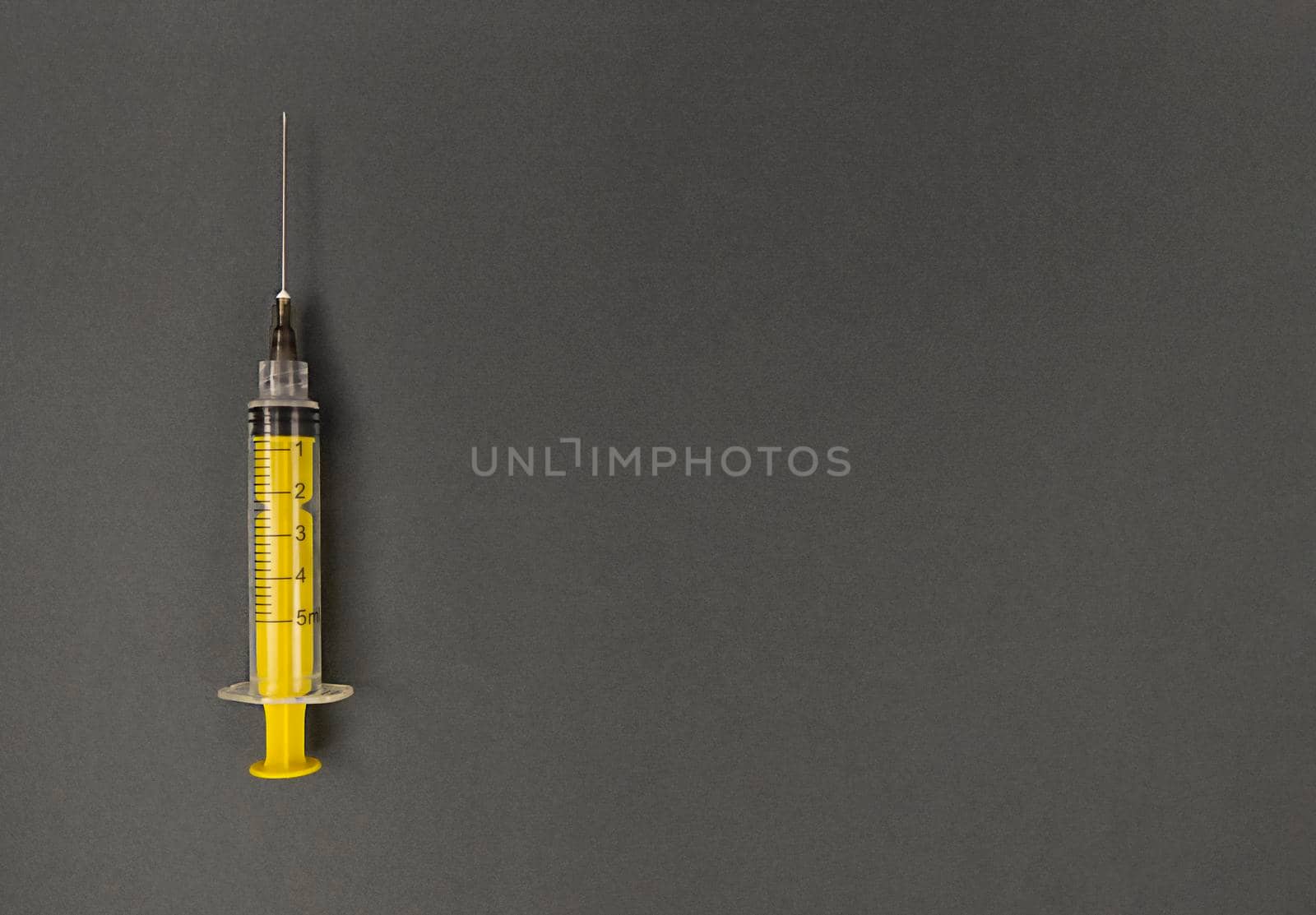 Yellow syringe on grey background. Simple flatlay with copy space.