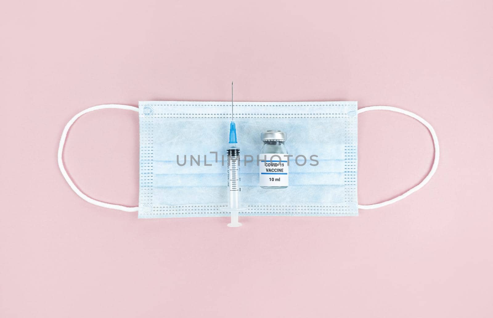 Syringe, medical bottle and face mask on a pink background.