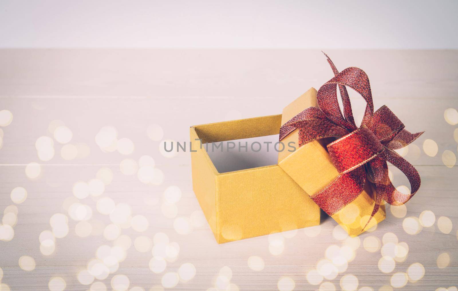 Gold gift box open on wooden table with bokeh background, love and romance, presents in celebration and anniversary with surprise on desk, happy birthday, copy space, nobody, valentine day concept.