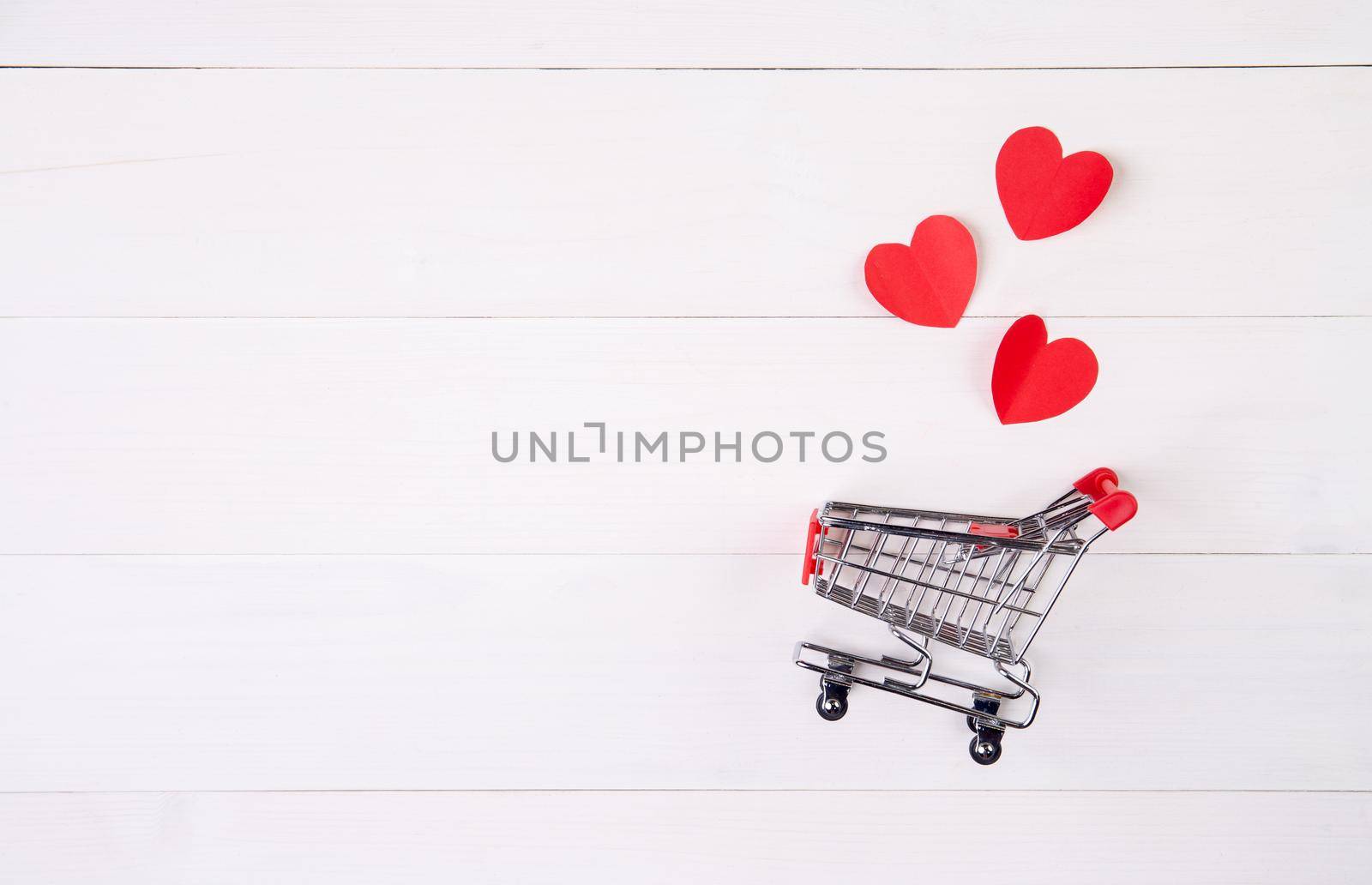 Shopping cart and heart shape paper on wooden table, sale concept in festive valentine day February 14, supermarket and store, symbol and celebration, commerce and selling in holiday concept. by nnudoo