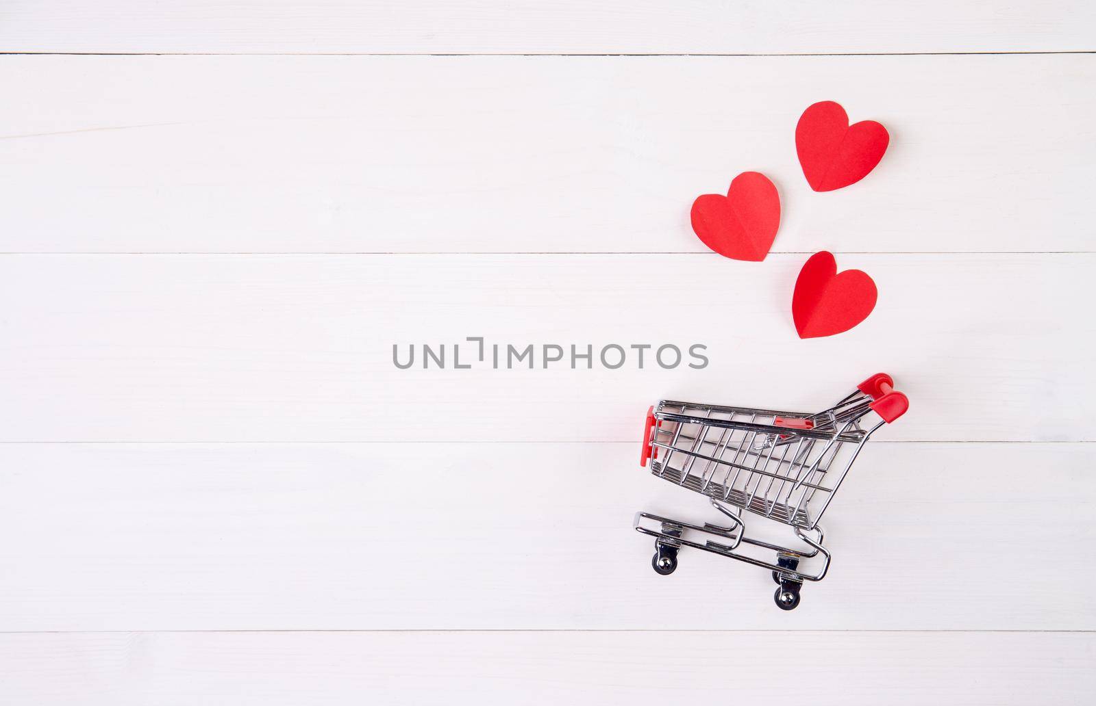 Shopping cart and heart shape paper on wooden table, sale concept in festive valentine day February 14, supermarket and store, symbol and celebration, commerce and selling in holiday concept.