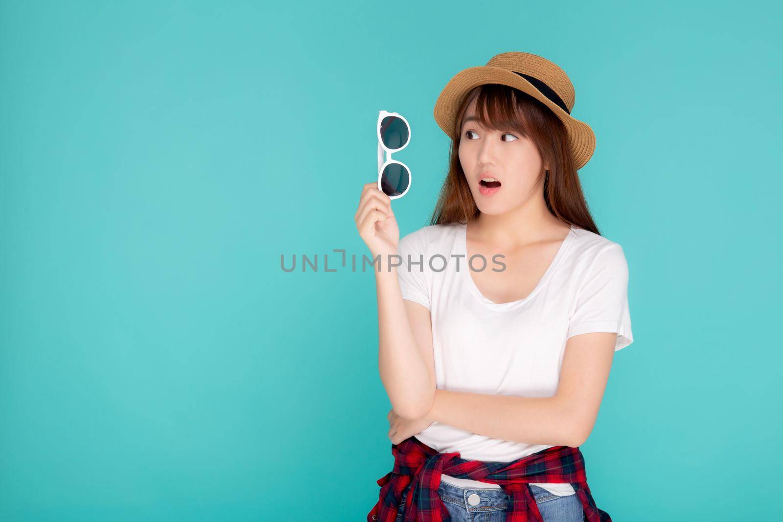 Beautiful portrait young asian woman wear hat and holding sunglasses excited and surprise journey summer trip in vacation isolated on blue background, tourist asia girl amazing with travel.