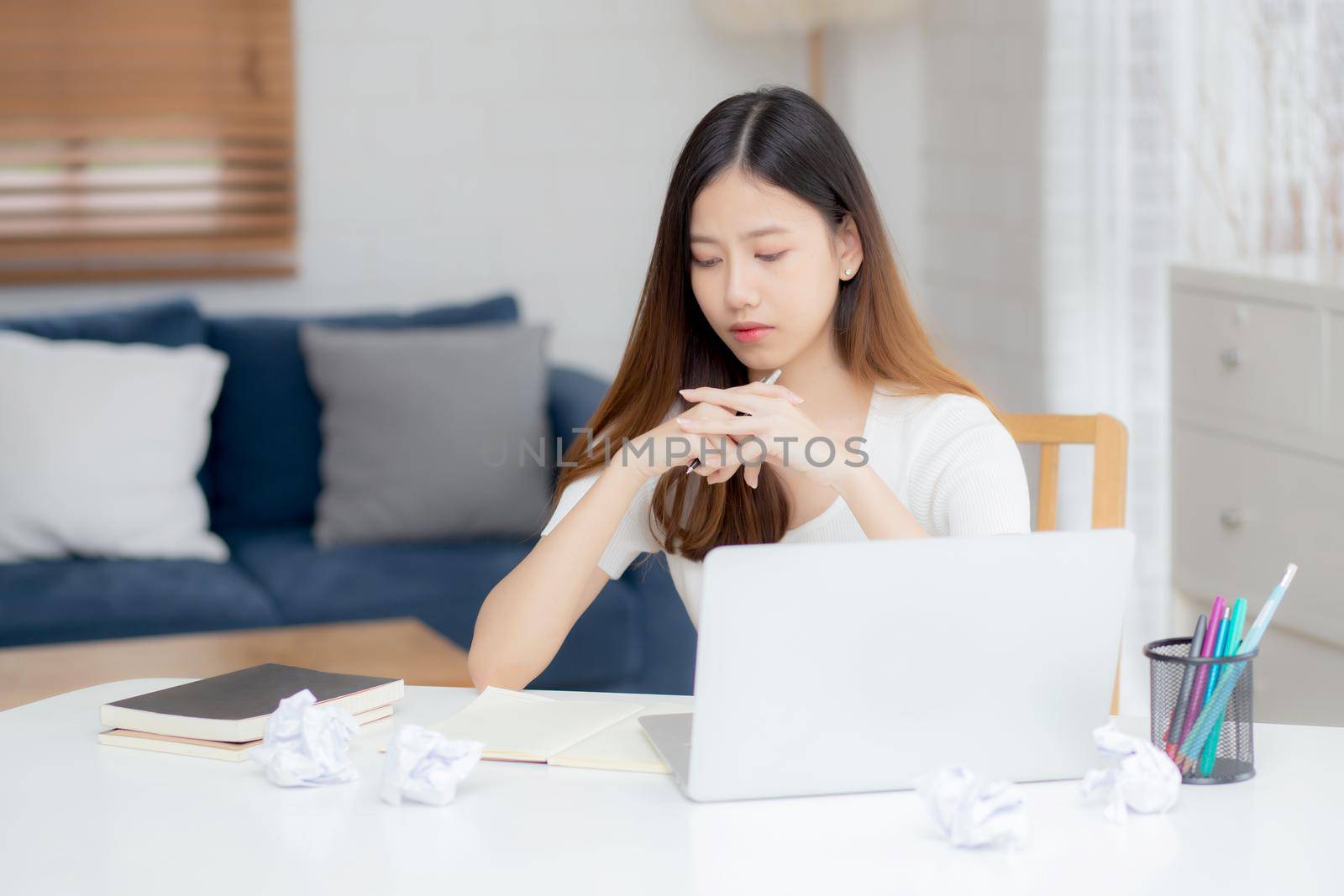 Young asian woman working with laptop computer think idea project and paper crumpled having problem on table at home, girl using notebook with frustrated and trouble, business and freelance concept.