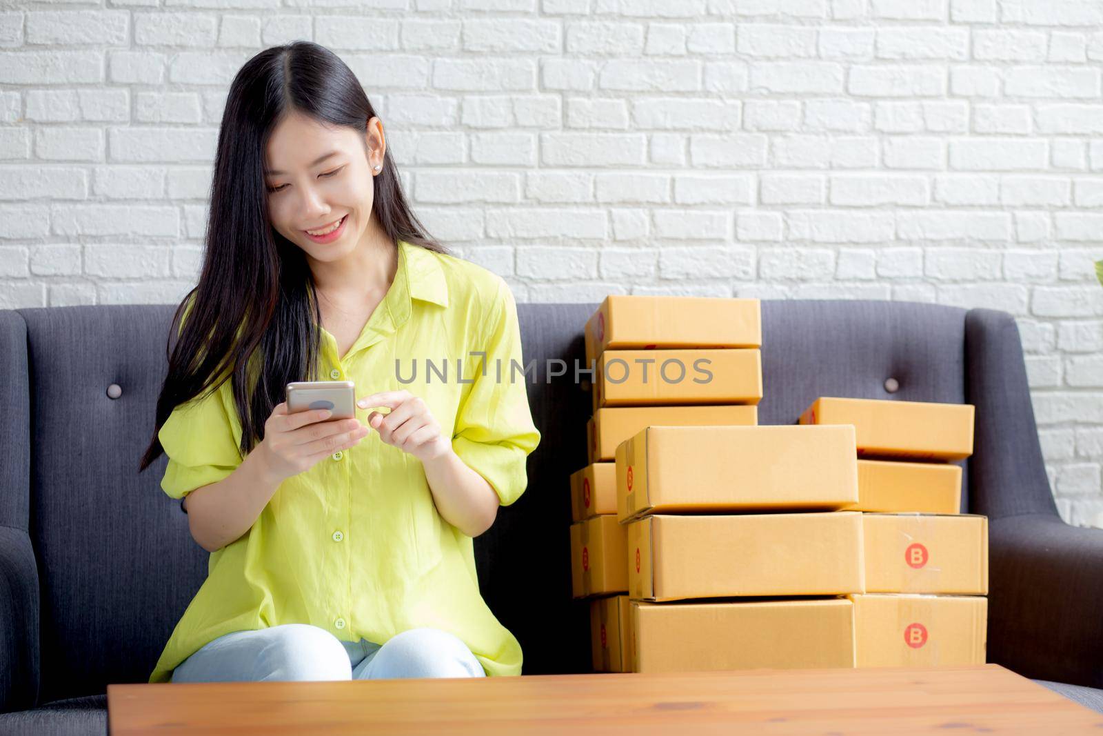 Young asian woman is entrepreneur check order from smartphone with customer while purchase online, logistic and delivery, online shopping, female is seller of business SME, merchant looking phone.