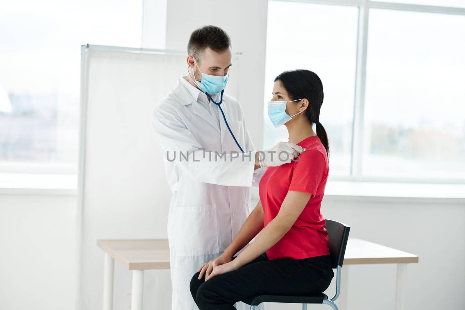 a doctor in a medical mask stands next to a woman in a red t-shirt chest examination breathing lungs. High quality photo