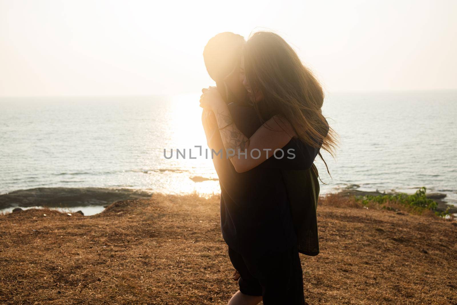 Backlit Portrait of a young romantic couple swirls in a hug against the backdrop of the sea. Anjuna Hills, Goa, India