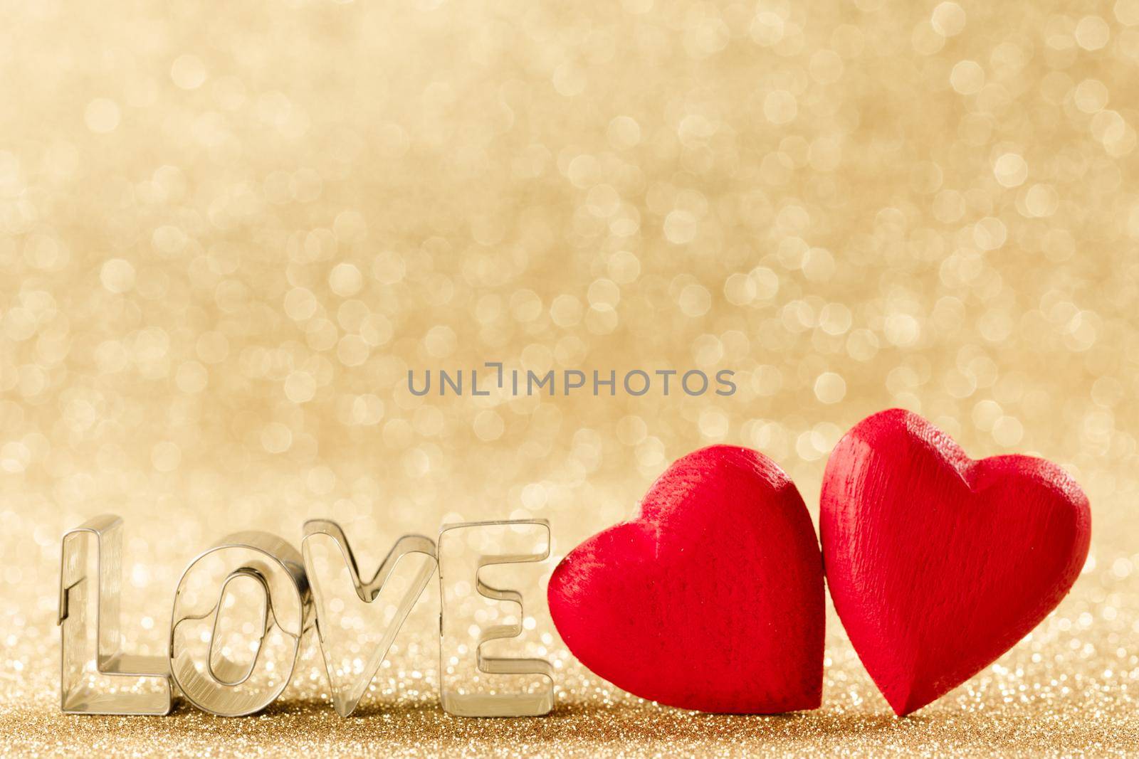 Two red handmade wooden hearts and word love on golden bright glitter lights bokeh background