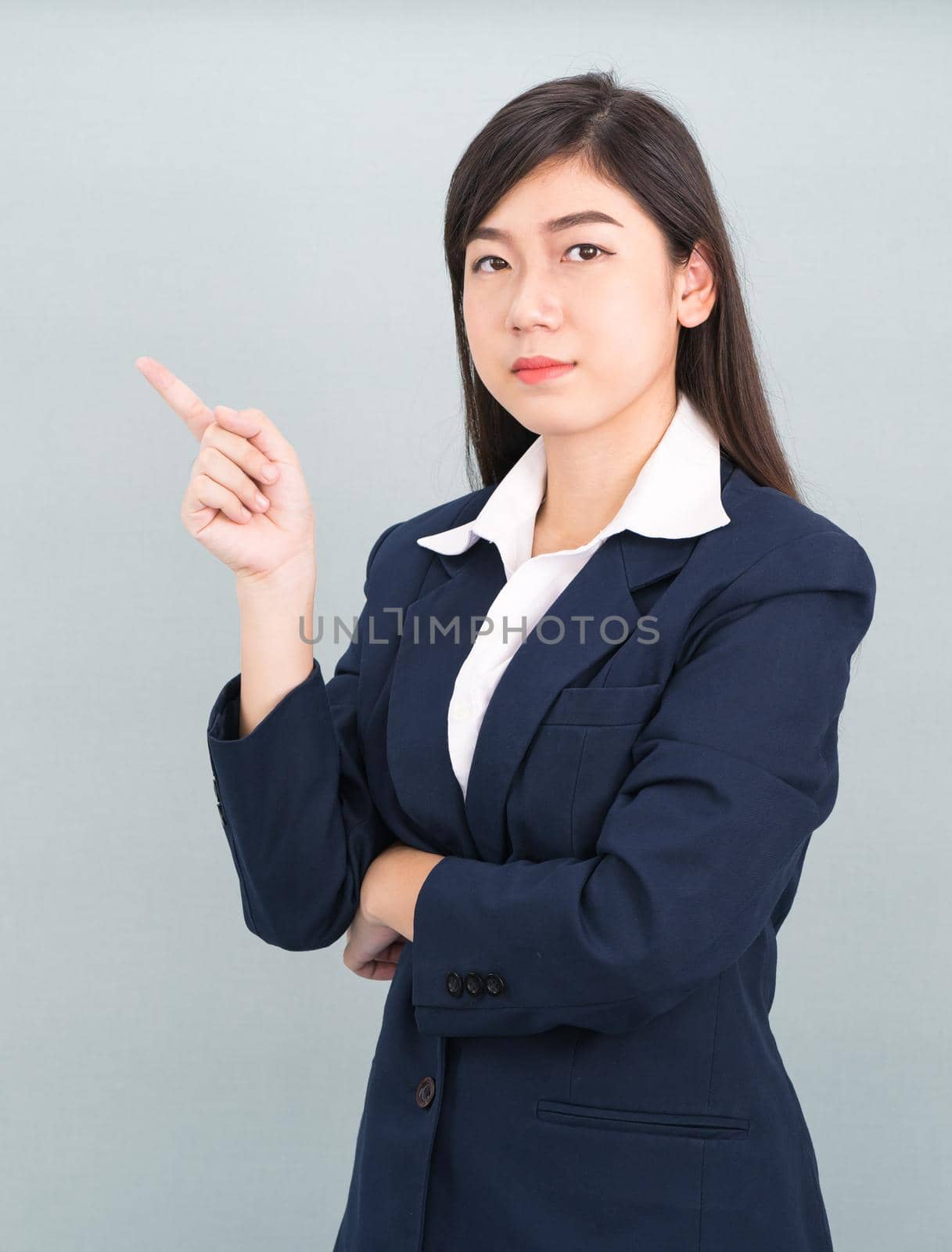 Asian businesswoman in suit with finger pointing up on gray background