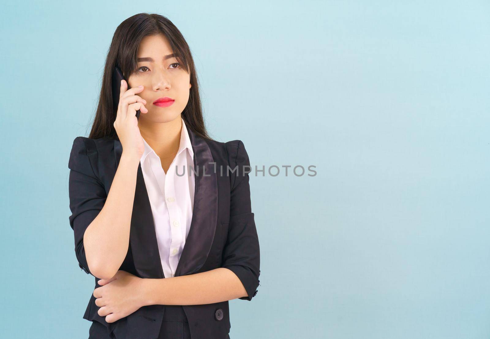 Young Asian women in suit standing posing using her phone against blue background