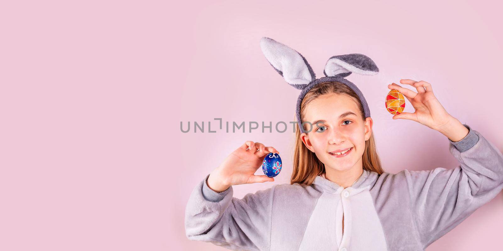 Girl in rabbit bunny ears on head with colored eggs on pink background. Cheerful smiling happy child. Easter holiday banner