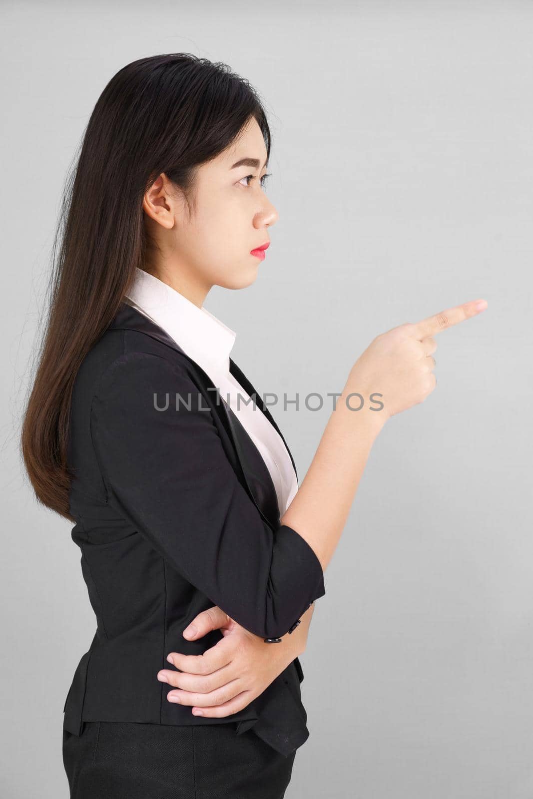 Asian woman in suit looking at camera and pointing finger on gray background