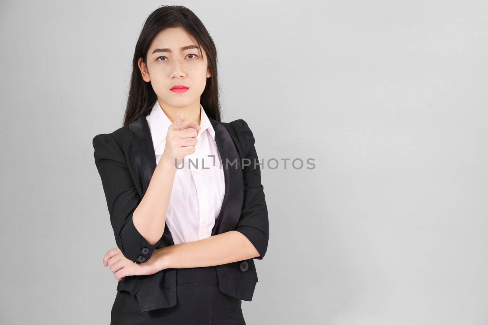 Asian woman in suit looking at camera and pointing finger on gray background