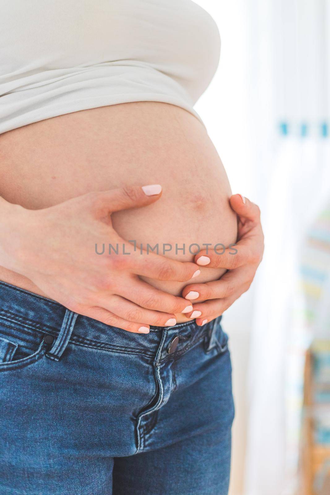 Caucasian pregnant mother touching her naked tummy, blue jeans, close up