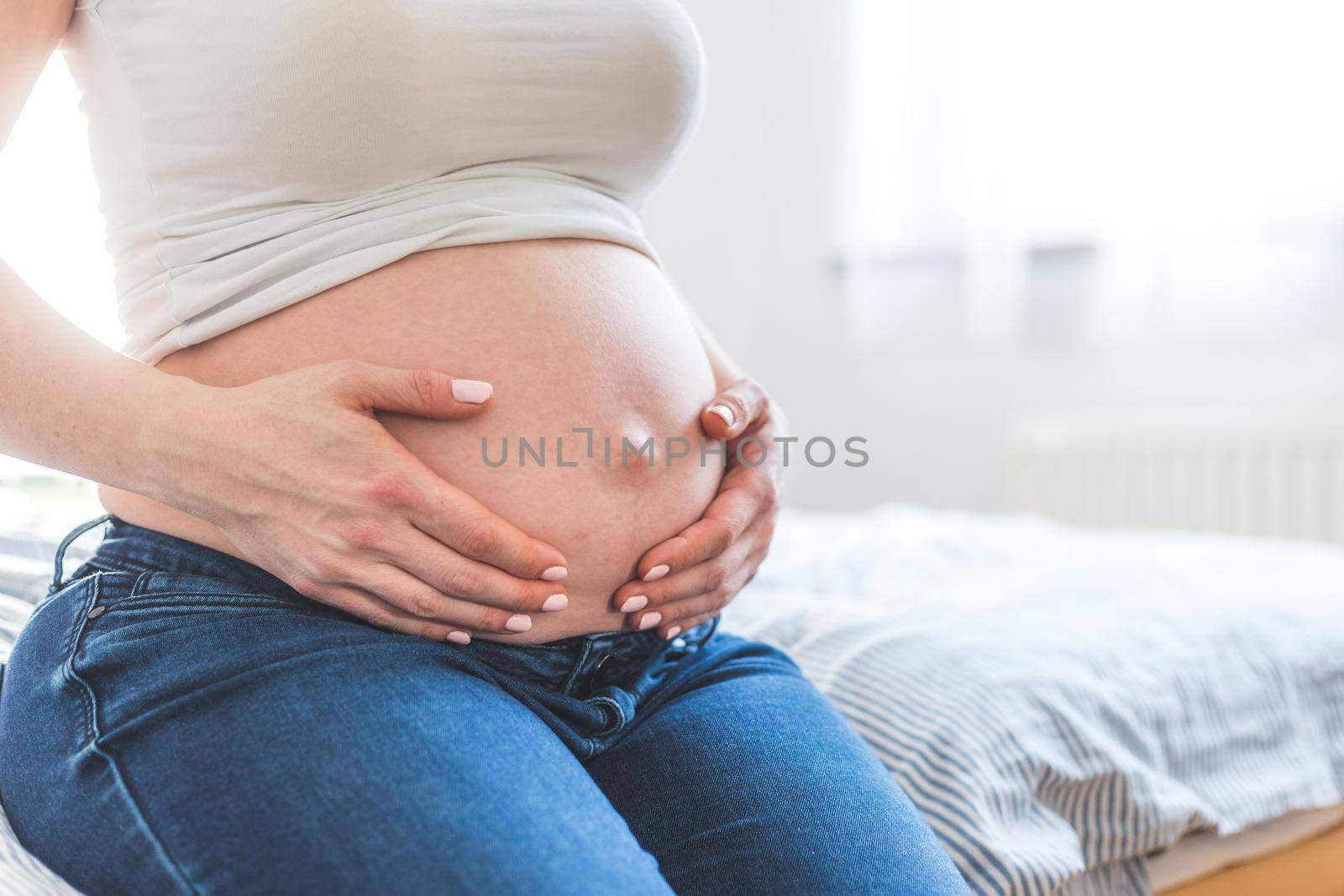 Caucasian pregnant mother touching her naked tummy, blue jeans, close up