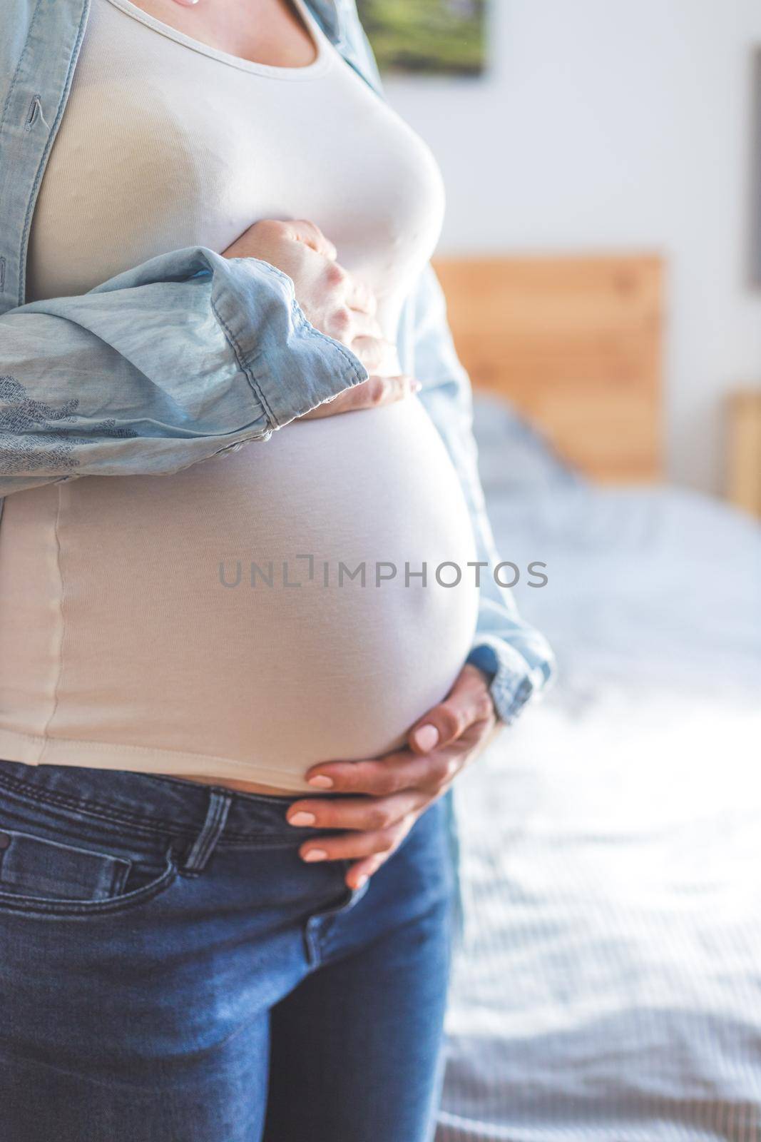 Caucasian pregnant mother touching her naked tummy, blue jeans, close up