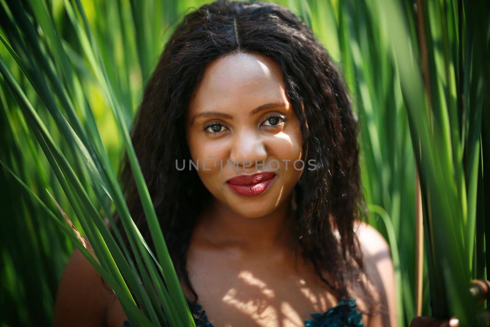 Cheerful young woman standing among tropical leaf.