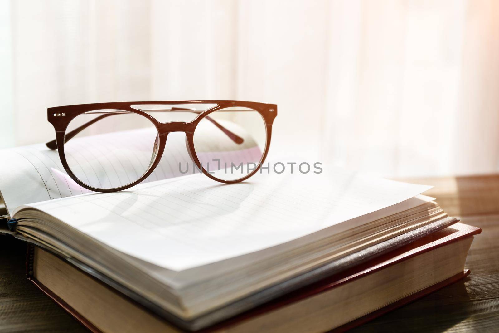 Reading glasses put on open books over wooden table beside the window