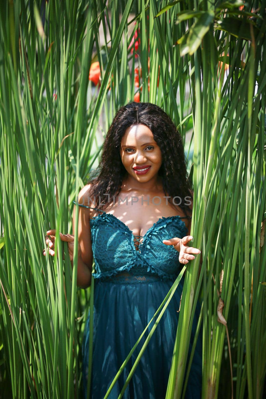 Cheerful young woman standing among tropical leaf.