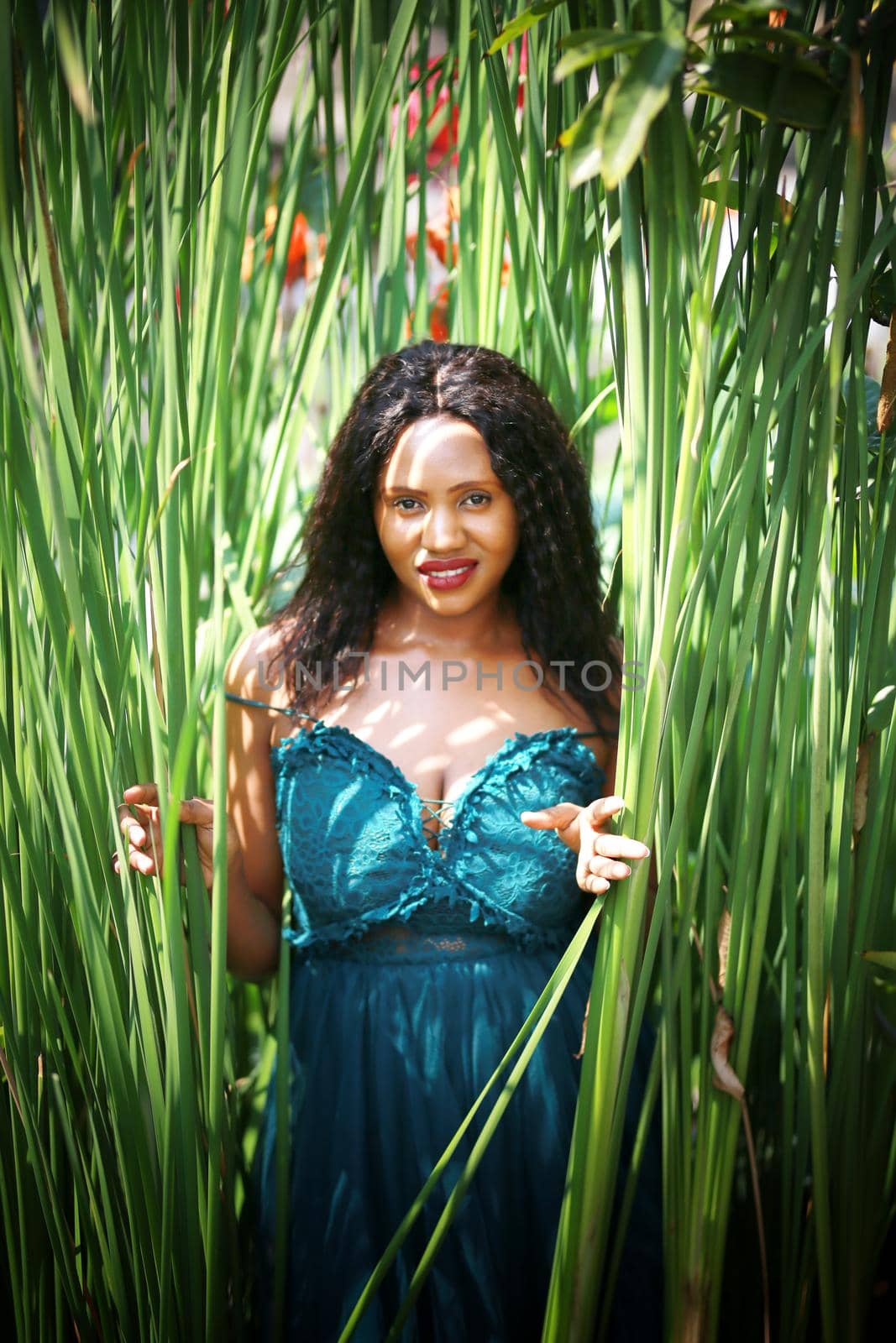 Cheerful young woman standing among tropical leaf.