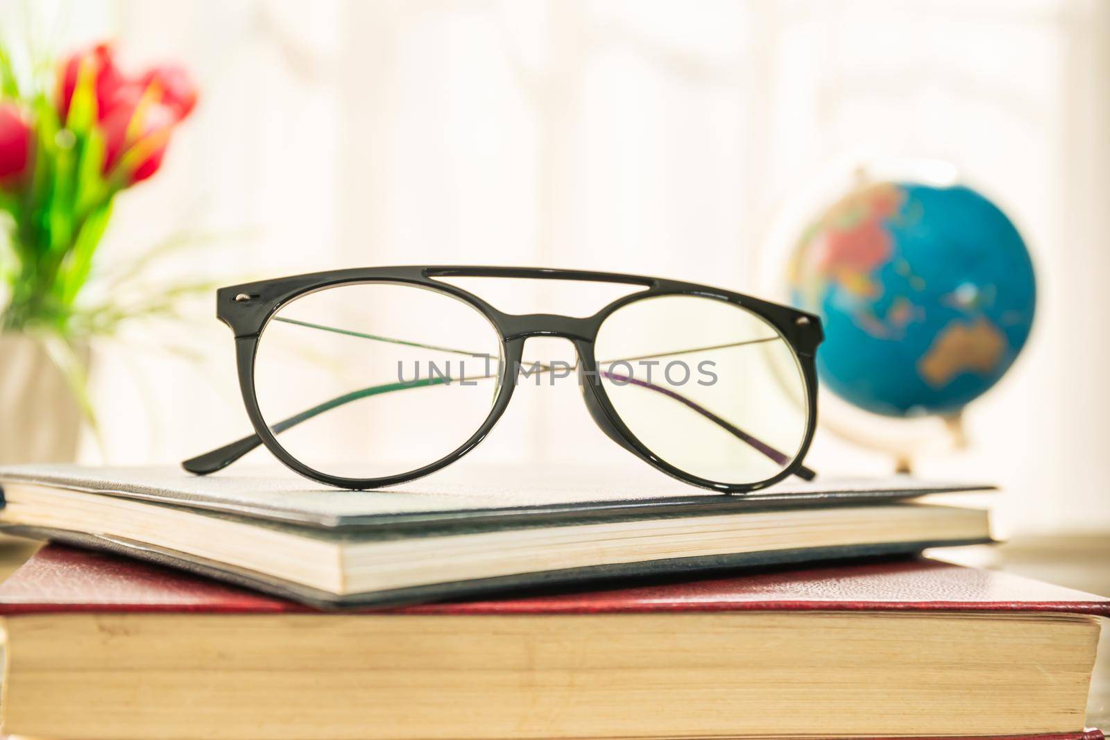 Reading glasses put on hardcover books over wooden table beside the window