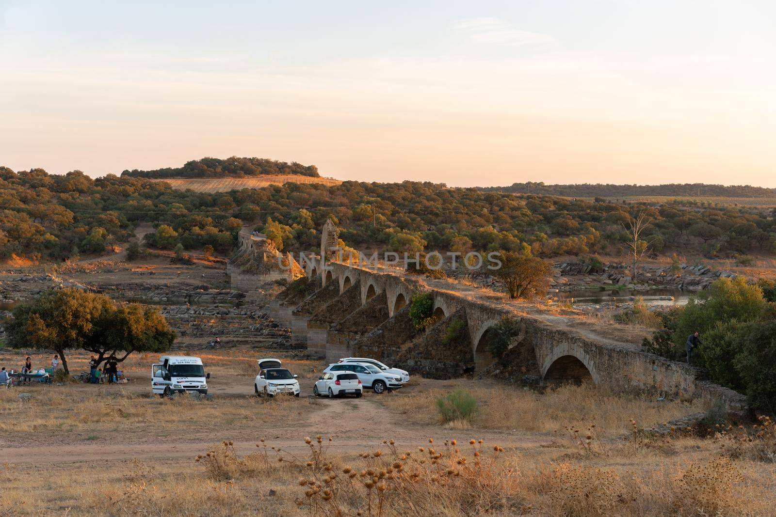 People having a picnic in Alentejo landscape with abandoned destroyed Ajuda bridge on the background at sunset, in Portugal