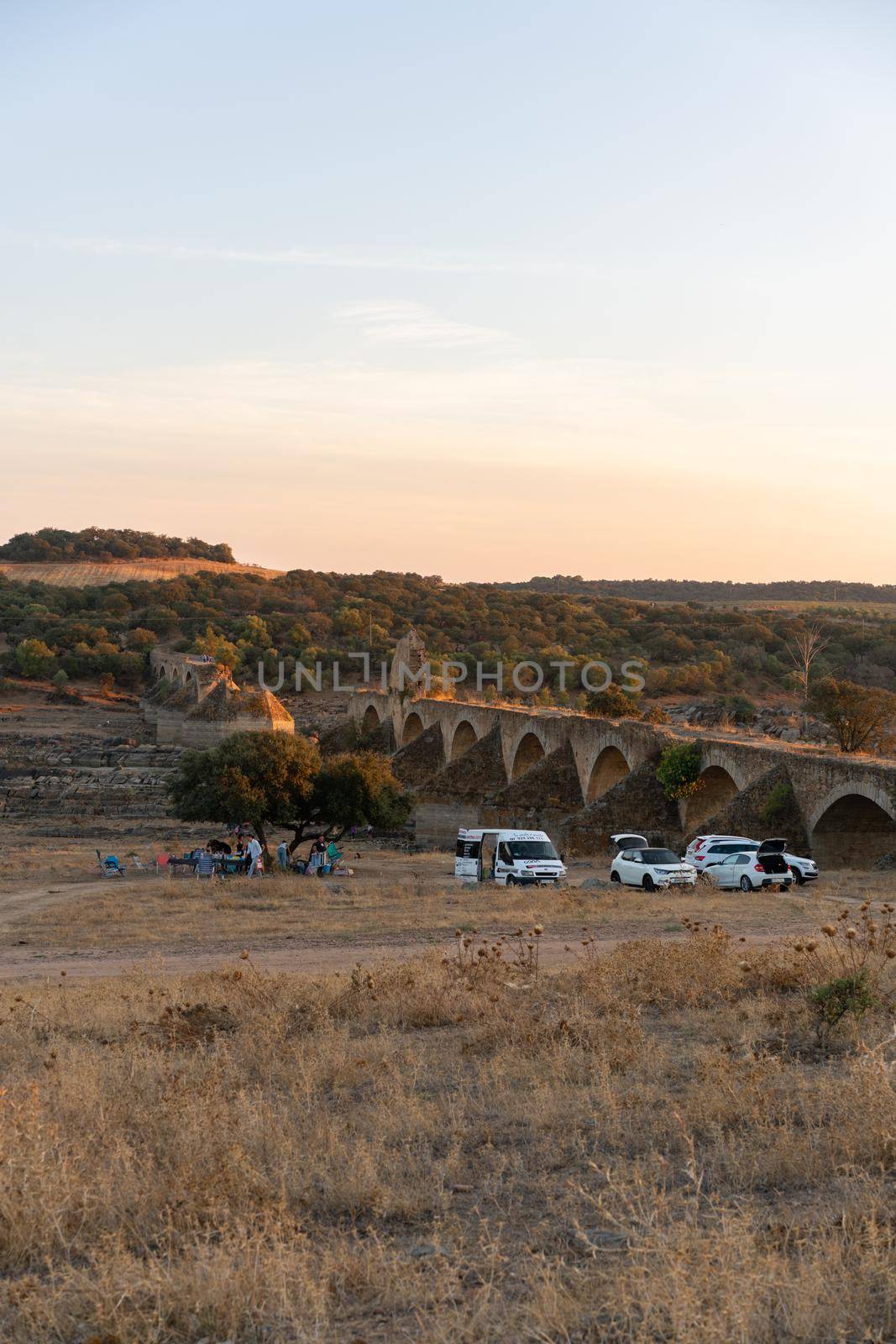 People having a picnic in Alentejo landscape with abandoned destroyed Ajuda bridge on the background at sunset, in Portugal