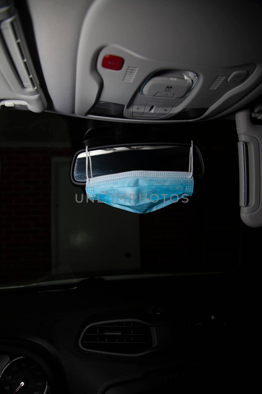 Blue medical mask hanging on a vehicle rearview mirror