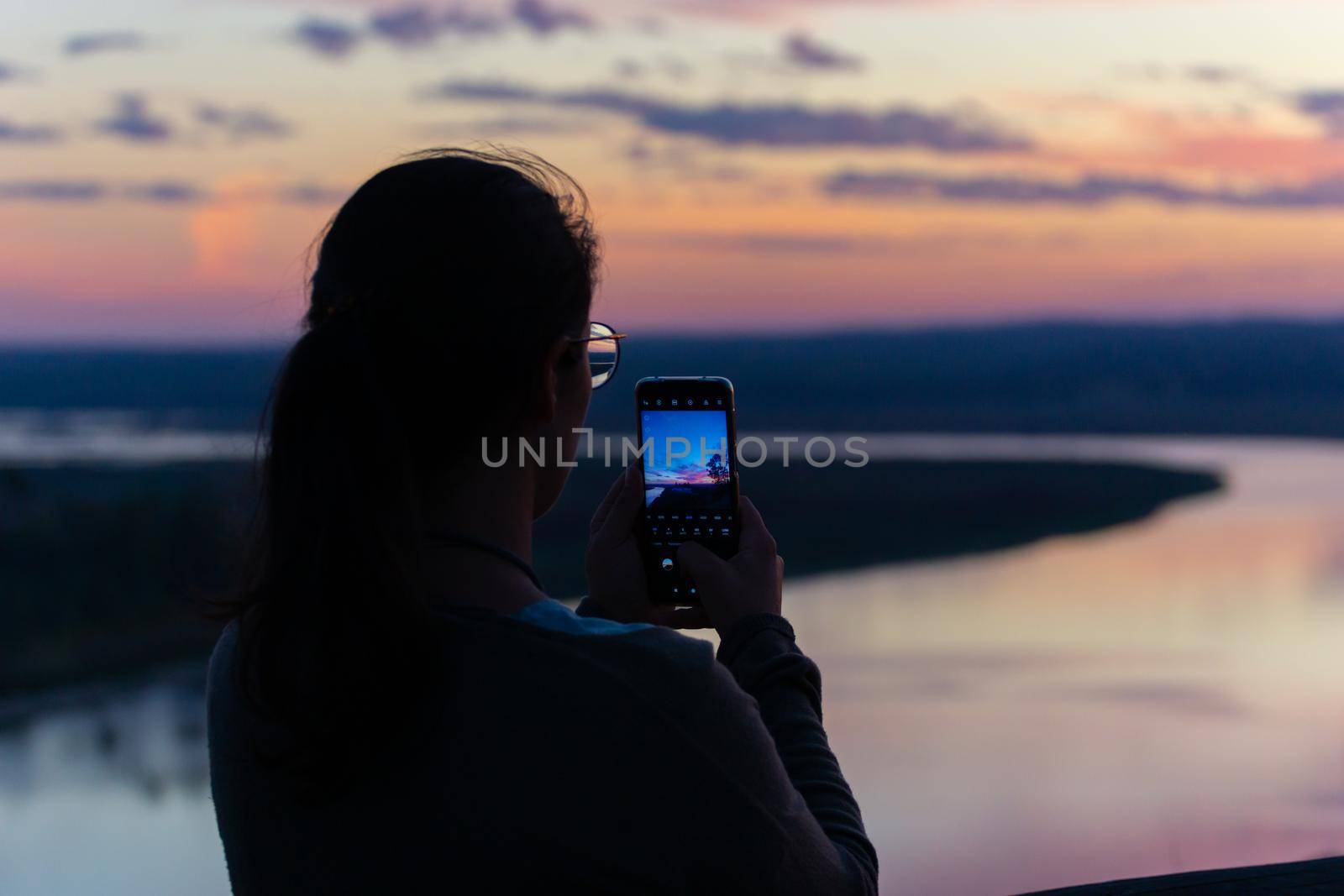 Woman photographing beautiful river landscape at sunset