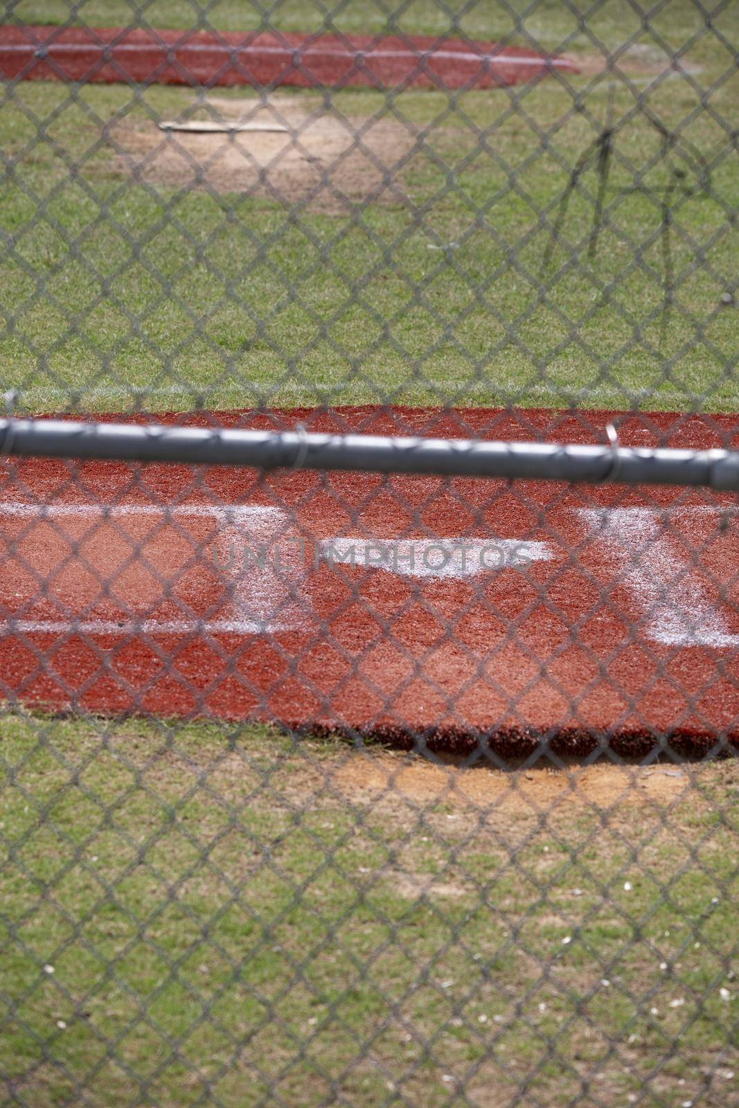 Home plate of an empty baseball field through a fence