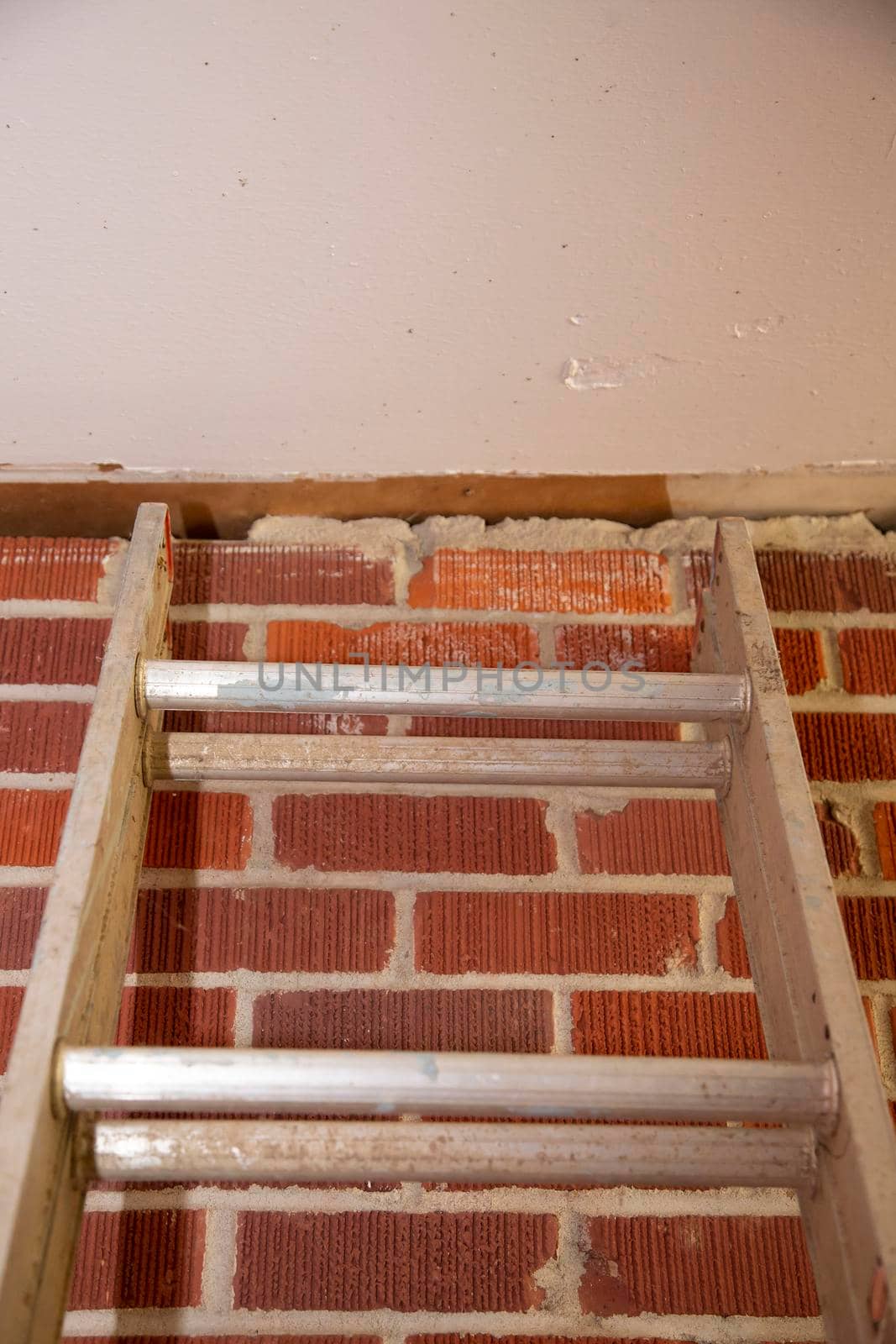 Top of a ladder against a red brick wall, leading to a ceiling