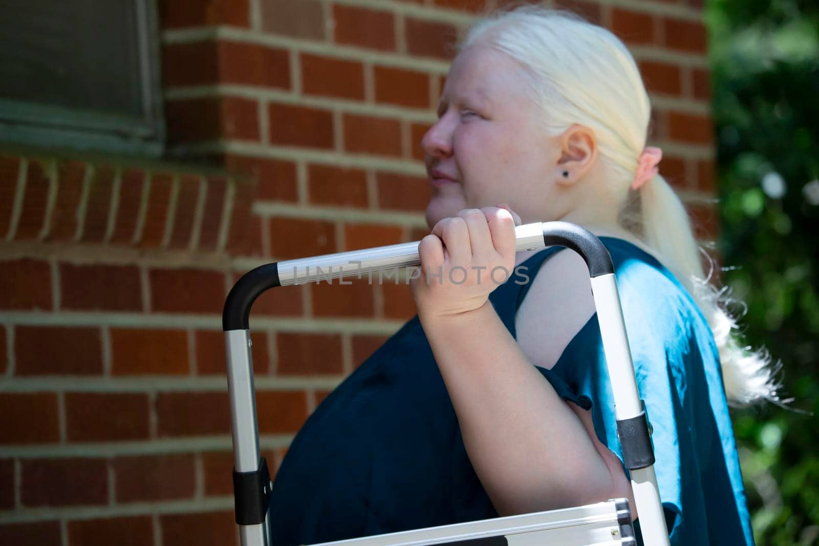 Legally blind woman carrying a step stool to the exterior wall of her home so that she can do home repairs