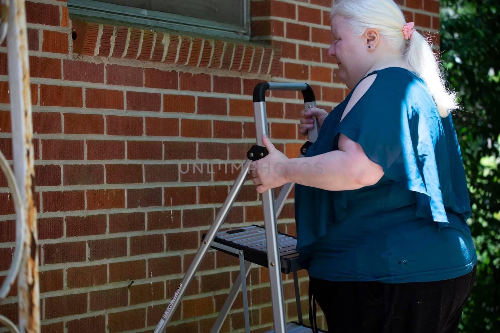 Albino woman setting up a step ladder near a red brick wall to look for necessary repairs