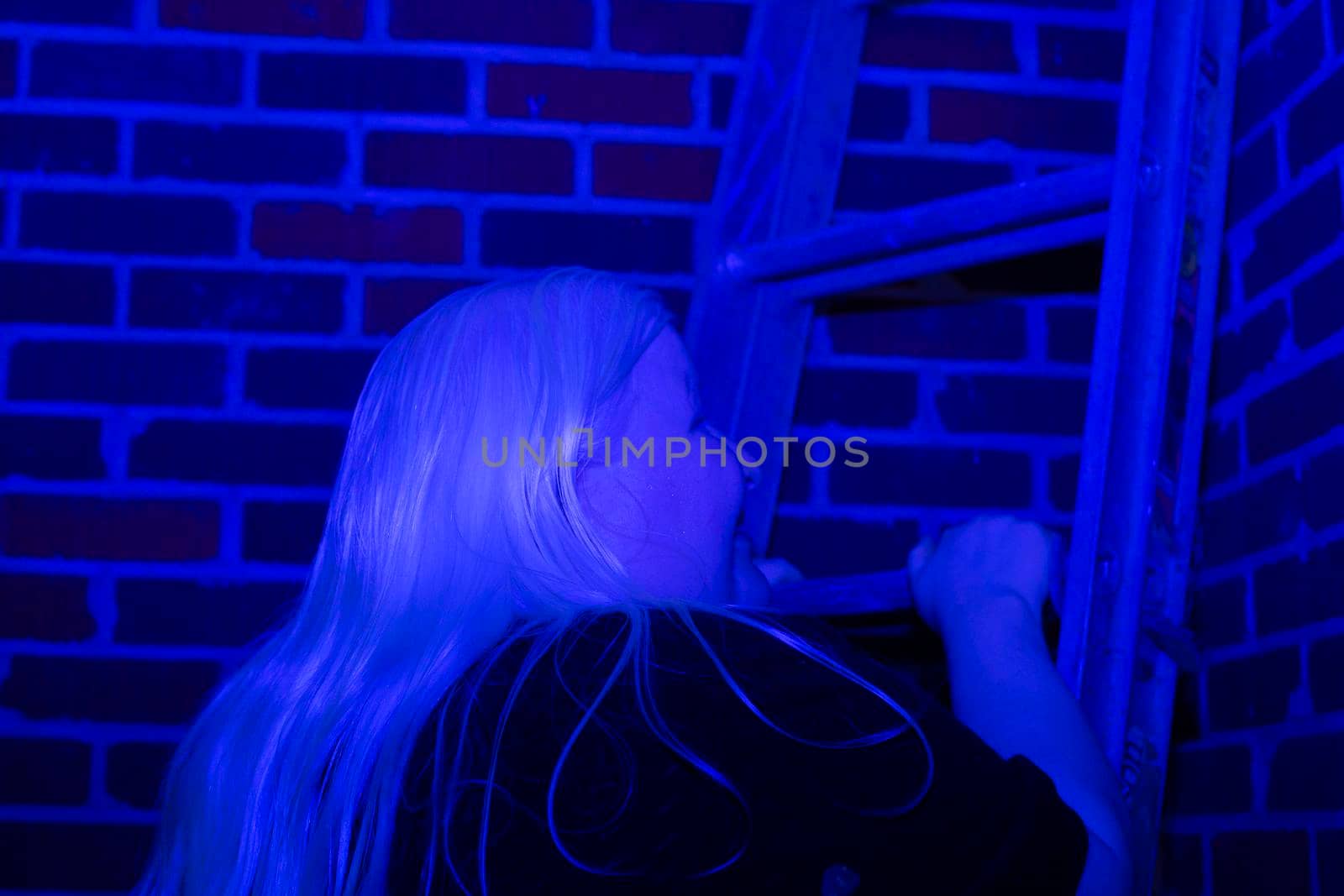 Woman climbing a ladder up a brick wall, covered in a blue hue