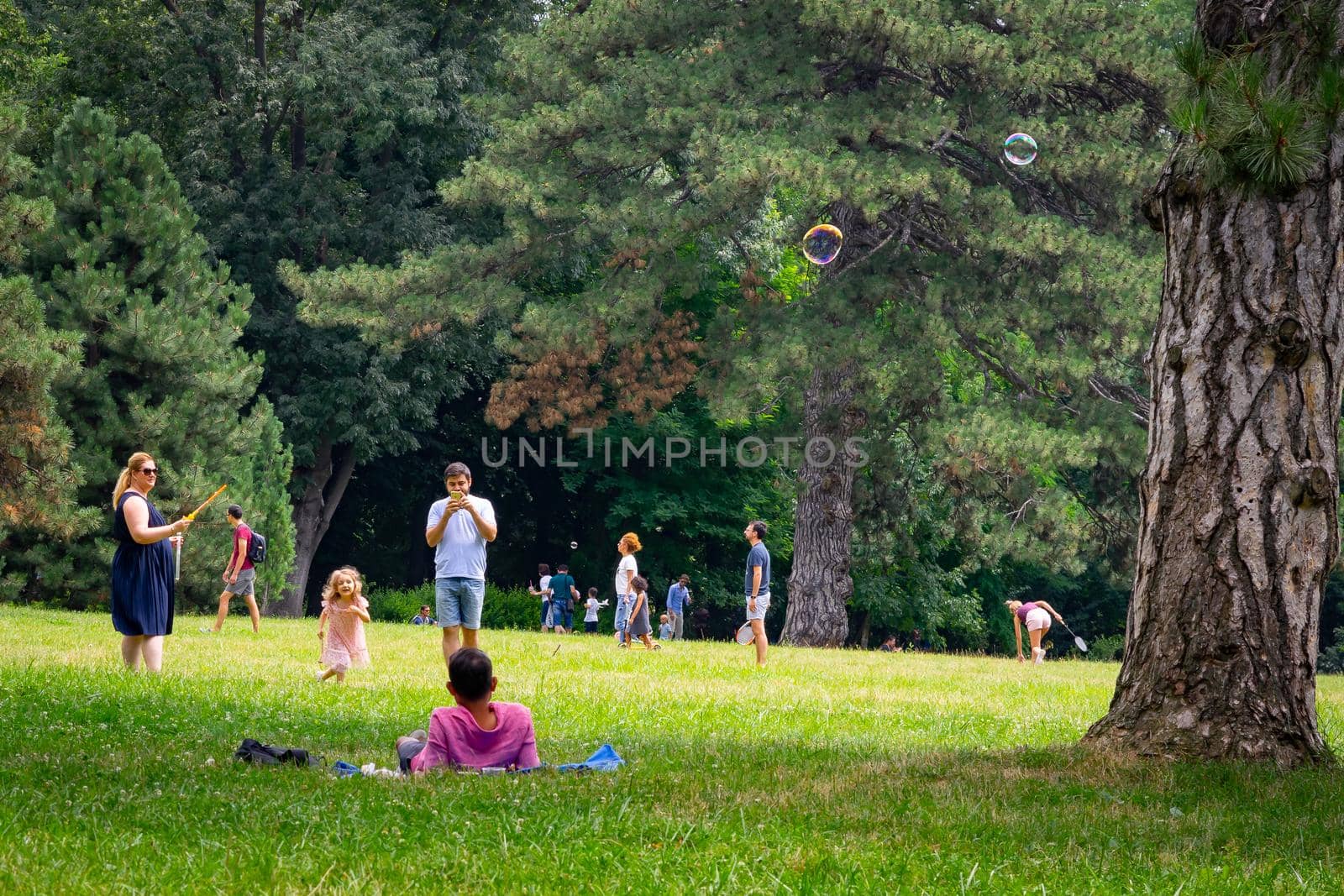 Mother making soap bubbles for herlittle daughter, people having picnic relaxing and having fun during coronavirus crisis in park and gardens of the domain from Mogosoaia in Bucharest, Romania, 2020. by vladispas