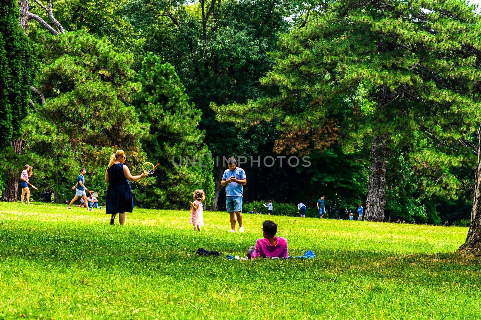 Mother making soap bubbles for herlittle daughter, people having picnic relaxing and having fun during coronavirus crisis in park and gardens of the domain from Mogosoaia in Bucharest, Romania, 2020. by vladispas