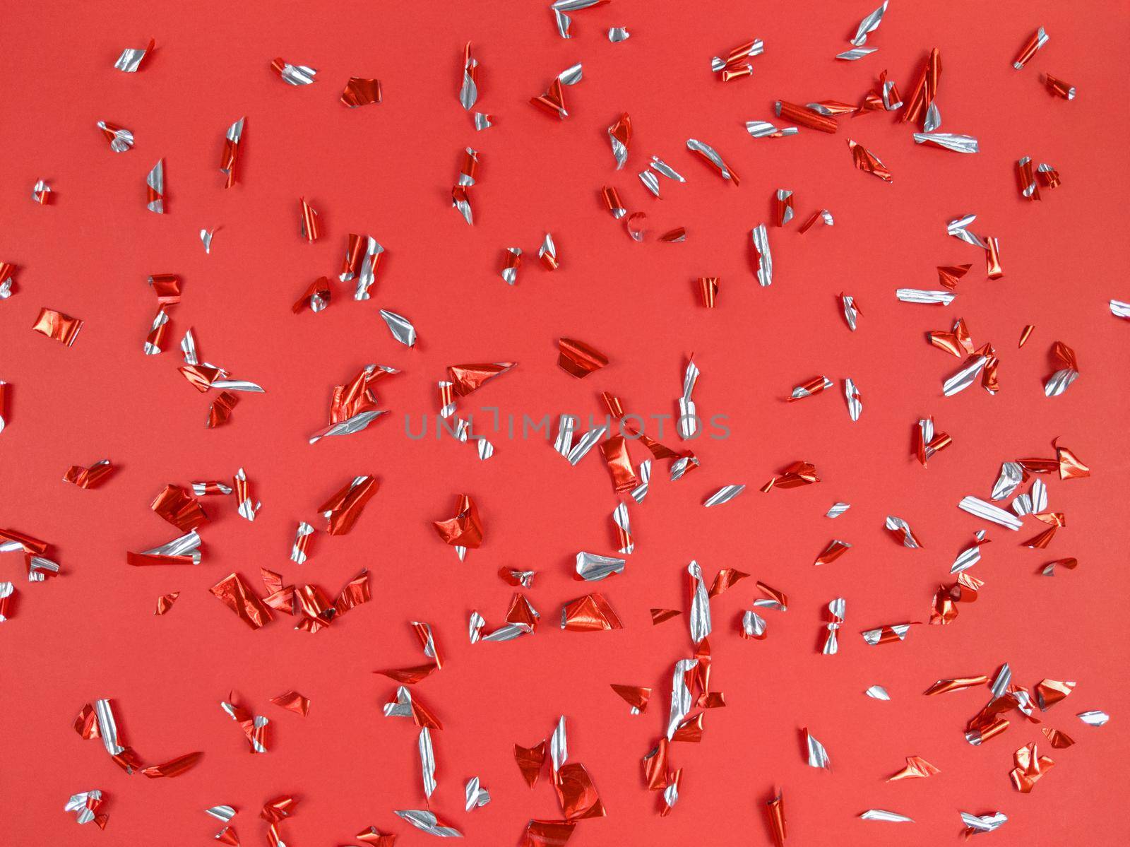 Confetti foil pieces on a red background. Abstract festive backdrop.