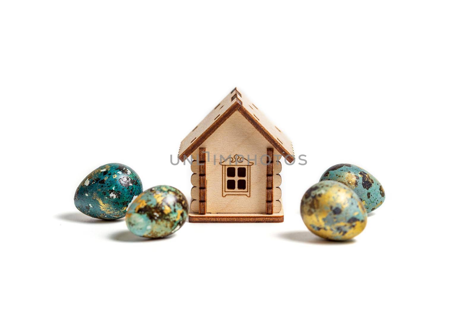 The concept of easter, ecology, respect for the planet: Children's toy wooden house and painted quail eggs next to it isolated on a white background