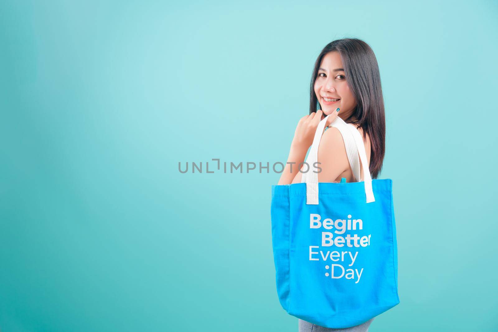 Asian happy portrait beautiful young woman standing smile her holding eco fabric cotton bag on hand and looking to camera on blue background with copy space for text