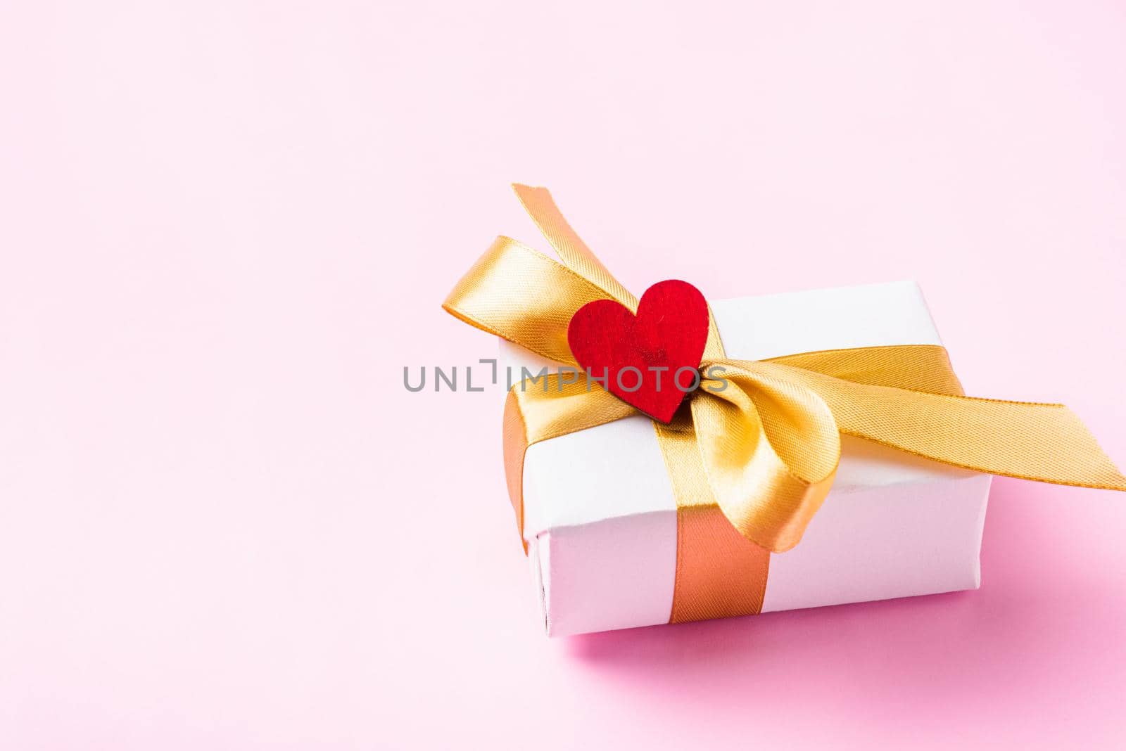 Valentines' day background concept. White gift box with a golden bow ribbon and wood red hearts composition greeting card for happy love isolated on pink background with copy space. View from above