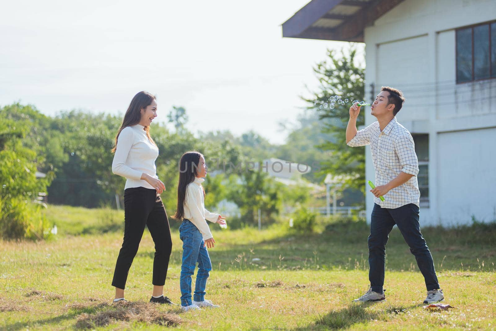 Asian family mother, father and little girl having fun together play blowing soap bubbles in park by Sorapop