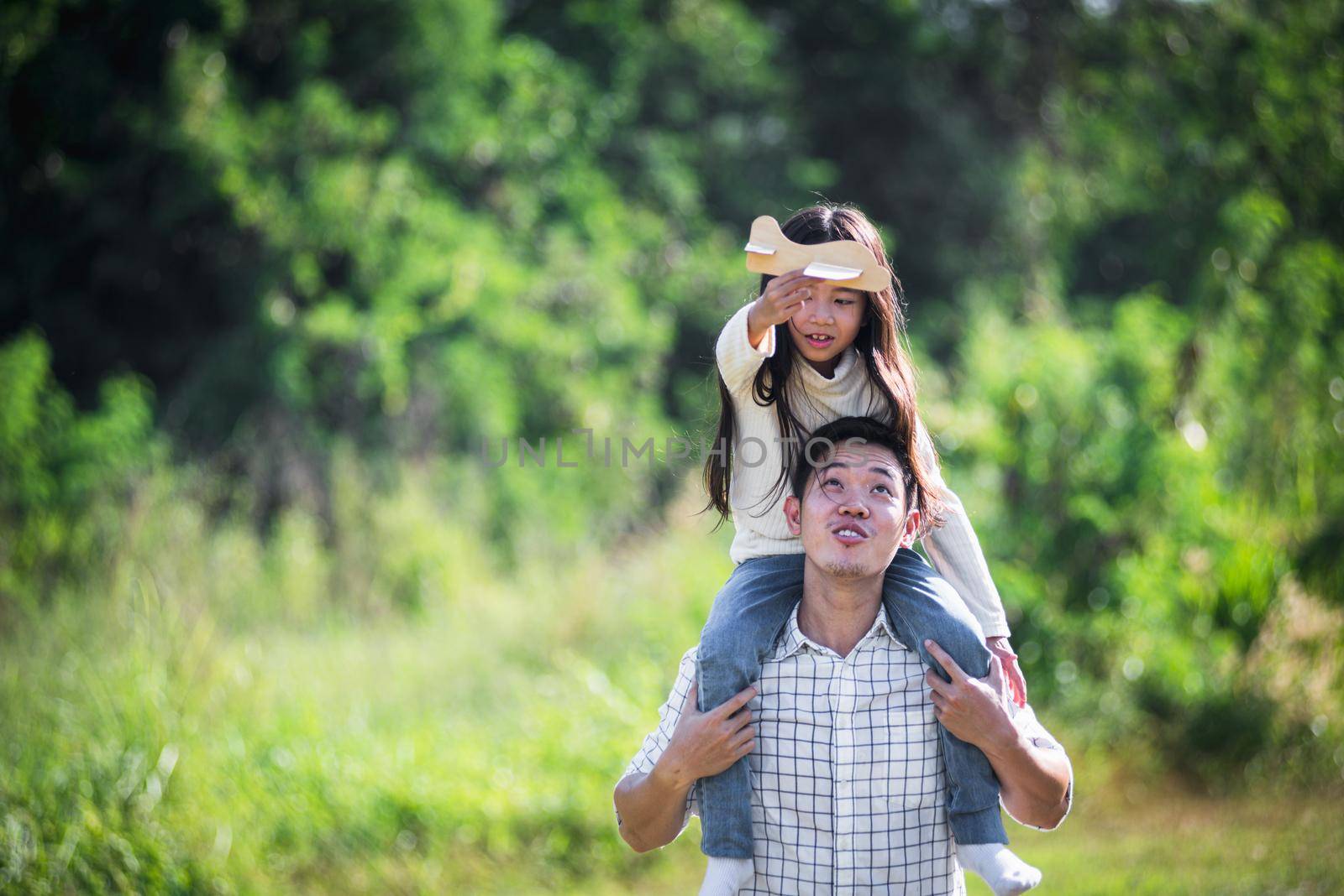 father and carrying an excited girl on shoulders having fun and enjoying outdoor lifestyle together playing aircraft toy by Sorapop