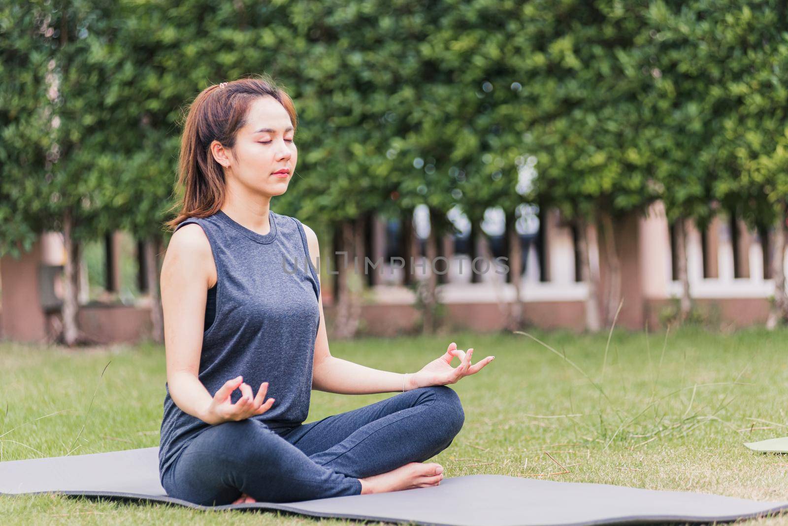 young woman doing yoga outdoors in meditate lotus pose by Sorapop