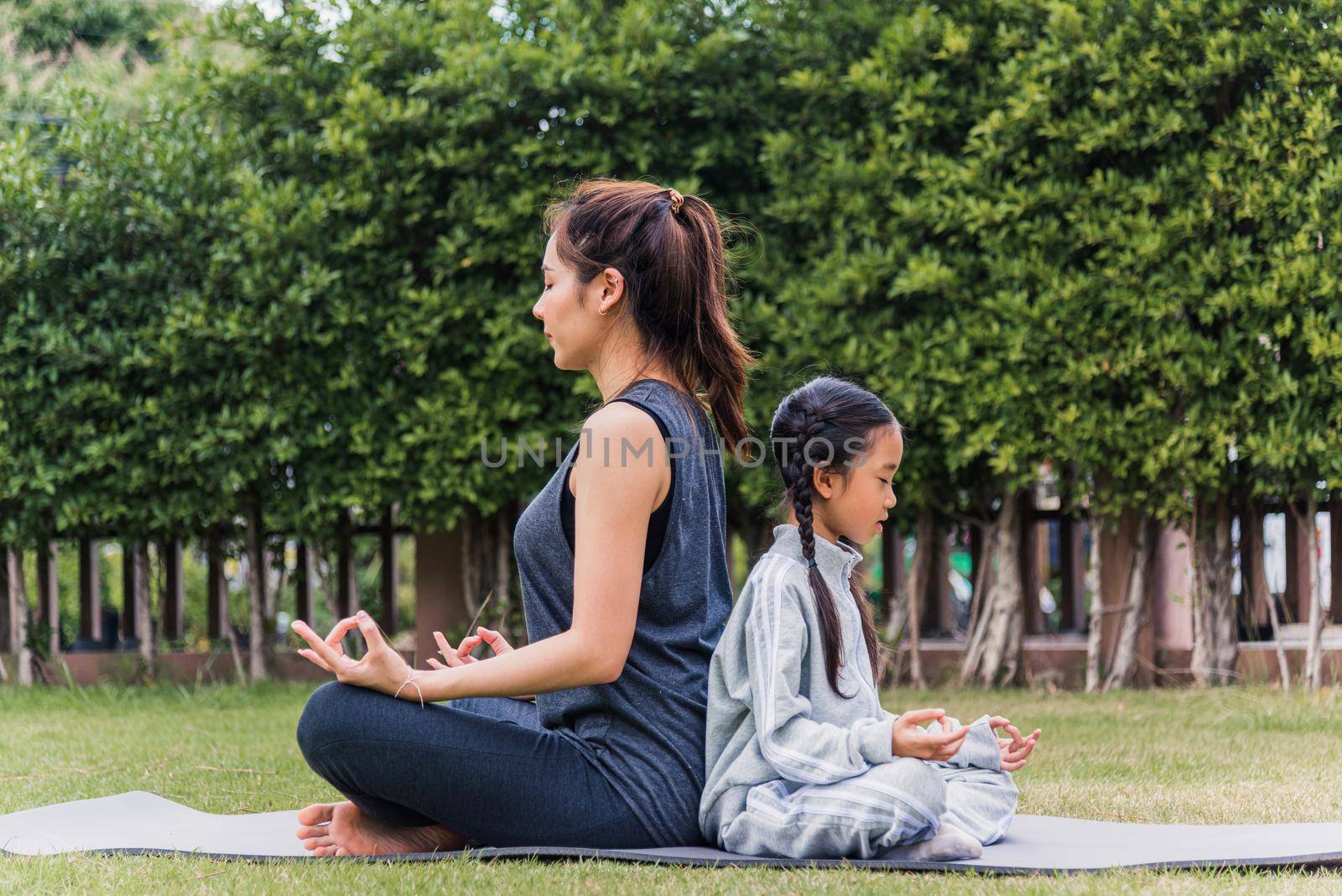 mother practicing doing yoga exercises with her daughter outdoors in meditate pose together by Sorapop