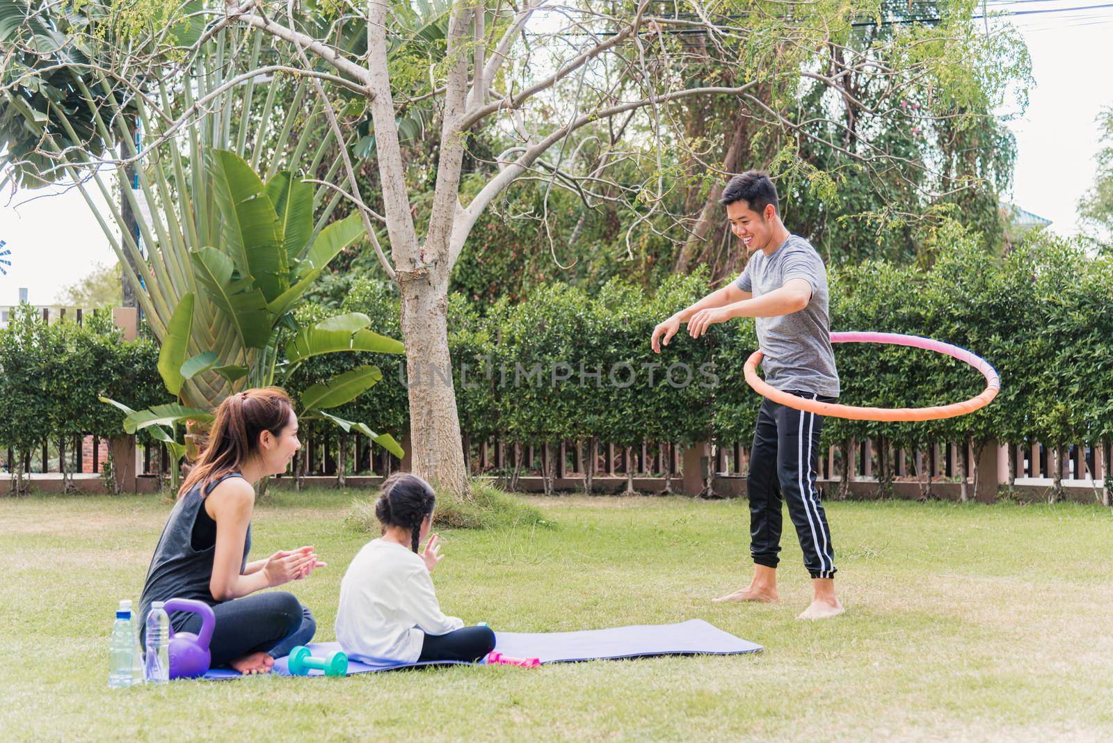 mother and child daughter practicing doing yoga exercises outdoors cheer father playing with hula hoops by Sorapop